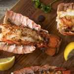 Lobster tails topped with alongside lemon slices and parsleyspices on cutter board