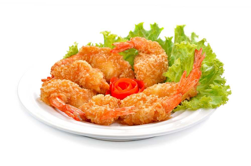 Fried shrimp with tails coated with bread crumbs serving with lettuce on a white plate