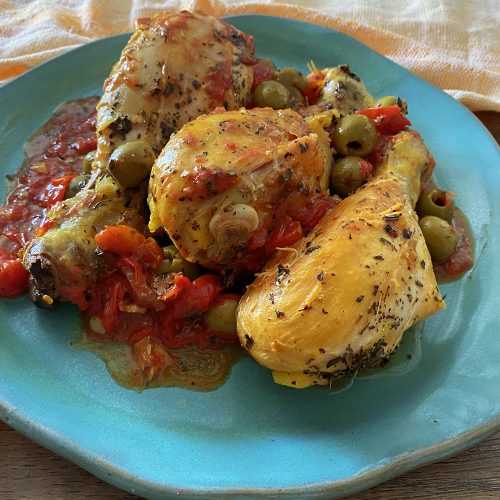 Three chicken drumsticks roasted with red sauce and green olives on blue plate