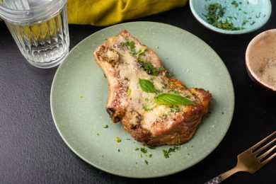 Pork chop topped with melted Parmesan cheese, parsley and basil top view