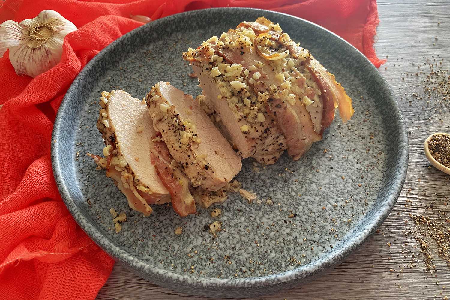 Pork loin slices topped with minced garlic and ground black pepper on a gray plate