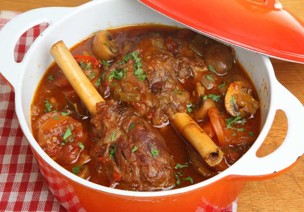 Lamb shanks in red sauce mixed with sliced mushrooms and topped with chopped parsley