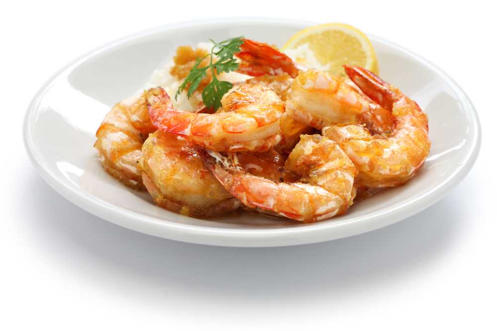 Fried shrimp in garlic sauce with parsley and slice of lemon in white plate