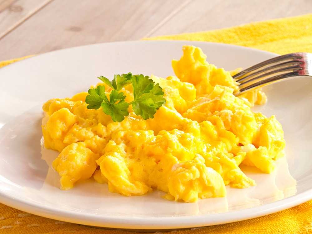 Scrambled Eggs with coriander leaves on top and a metal fork on a white plate