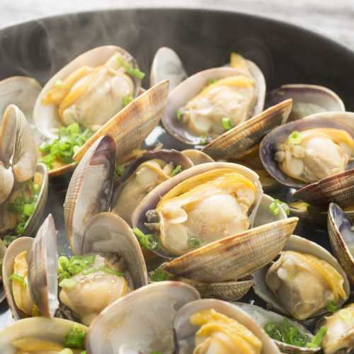 Steamed Clams in a black pan with smoke on top garnished with chopped scallion