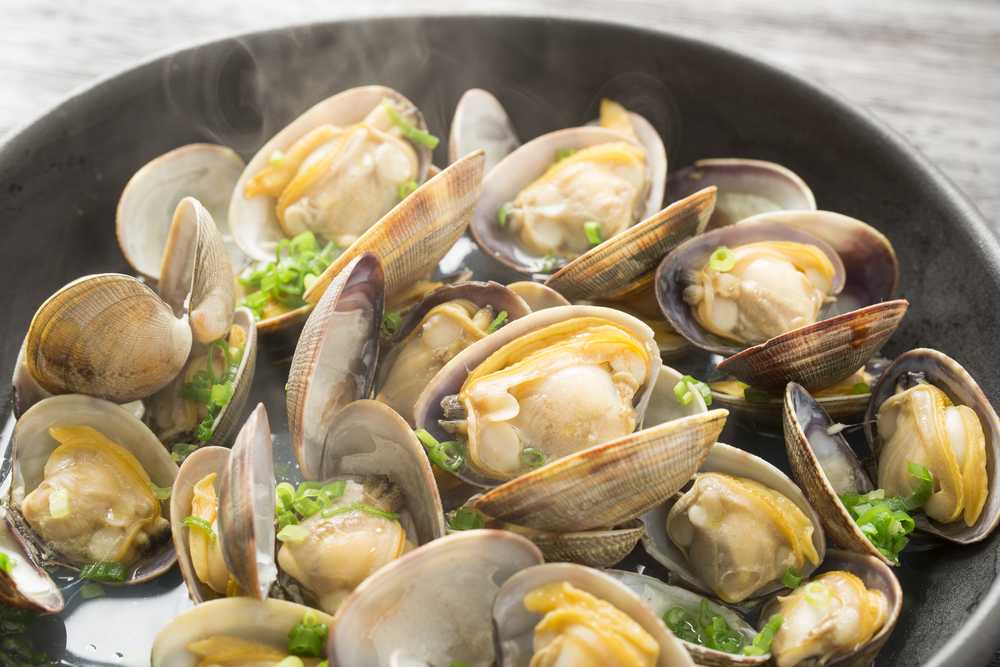 Steamed Clams in a black pan with smoke on top garnished with chopped scallion