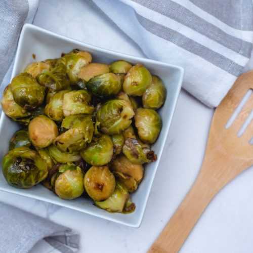Roasted brussel sprouts in a square white bowl near a woםden spatula