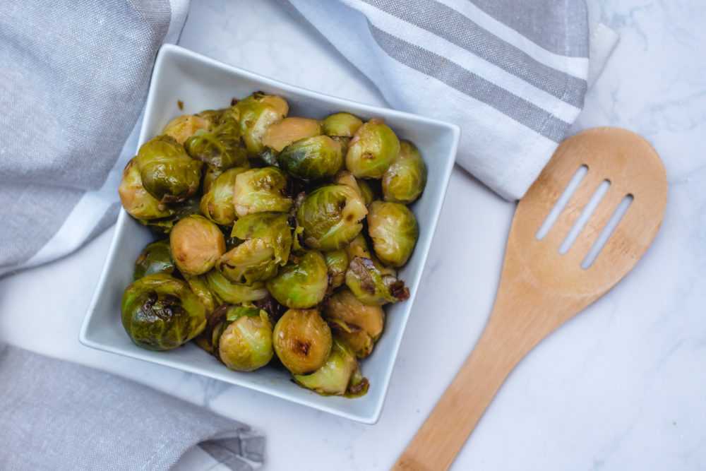 Roasted brussel sprouts in a square white bowl near a woםden spatula 