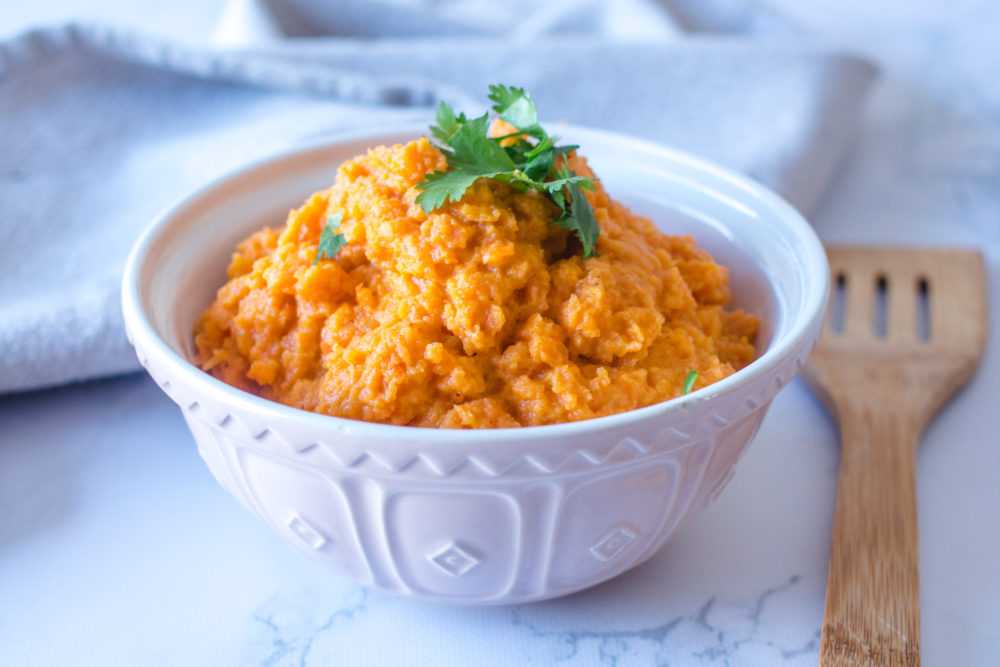 Carrot mash in a white bowl topped with parsley