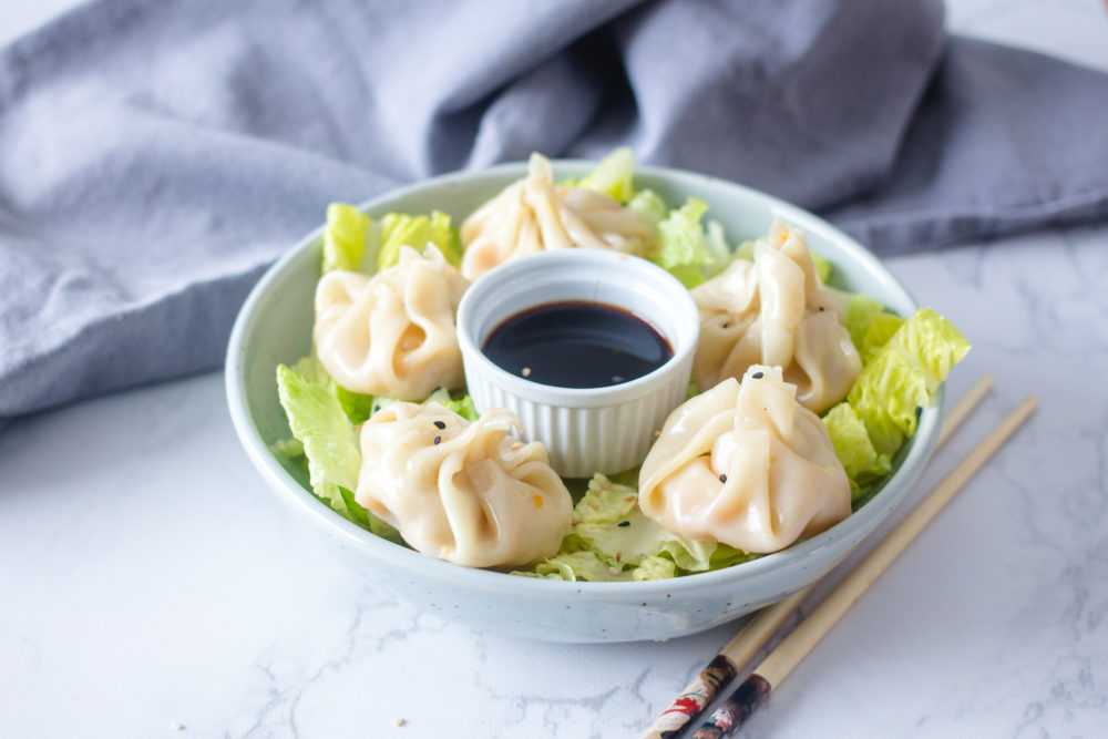 Five chicken dumplings on shredded lettuce with small bowl of soy sauce and chopsticks on side