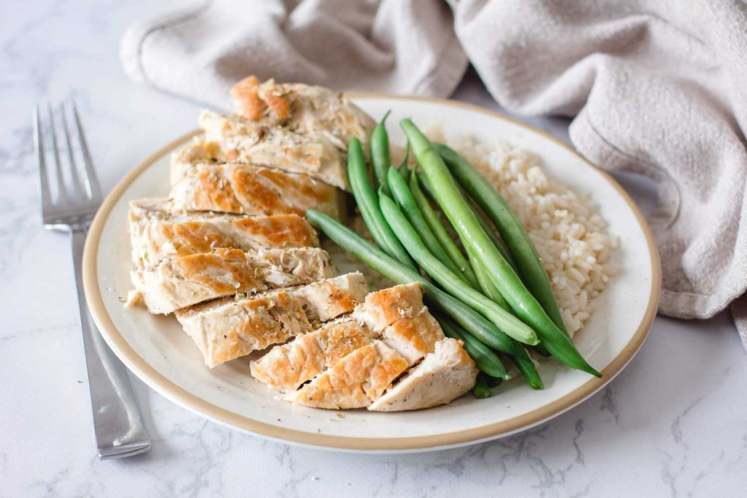 Chicken breasts slices topped with spices alongside whole green bean and jasmine rice