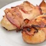 Yummy grilled chicken breasts wrapped win crispy bacon on white plate