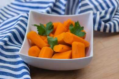 Chopped carrot pieces in a white square bowl with parsley on top