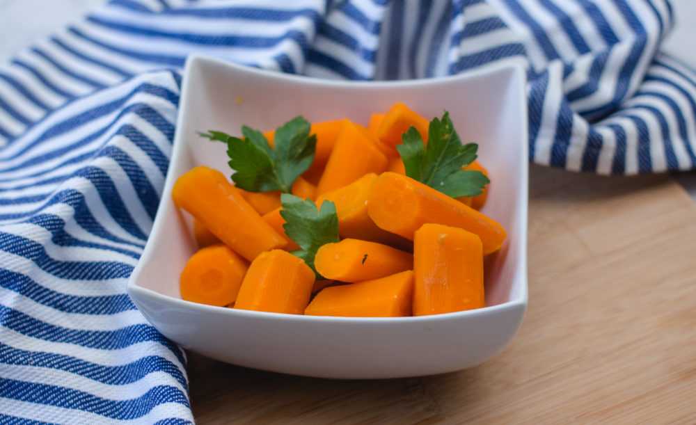 Chopped carrot pieces in a white square bowl with parsley on top