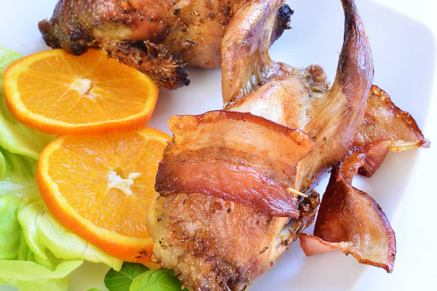 Roasted quail wrapped with bacon with orange slices and lettuce on side