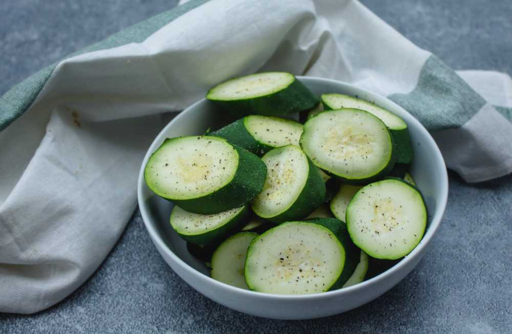 Steamed zucchini slices topped with kosher salt and black pepper in white bowl