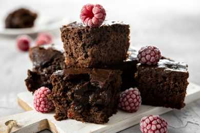 4 chocolate brownies topped with raspberry on a white cutting board