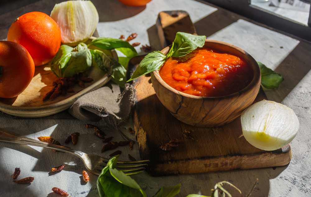 Wooden bowl filled with Arrabiata sauce with basil, tomatoes and onion on side