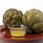 Two cooked artichokes in a brown plate near a buttery sauce