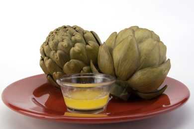 Two cooked artichokes in a brown plate near a buttery sauce