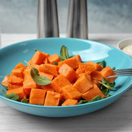 cooked sweet potato cubes with mint leaves in a blue bowl