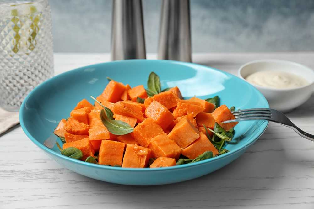 cooked sweet potato cubes with mint leaves in a blue bowl