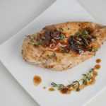 chicken breast topped with maple sauce and spices on a white square plate top view