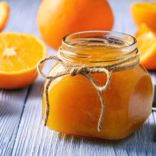 Orange jam in a small jar alongside fresh orange slices