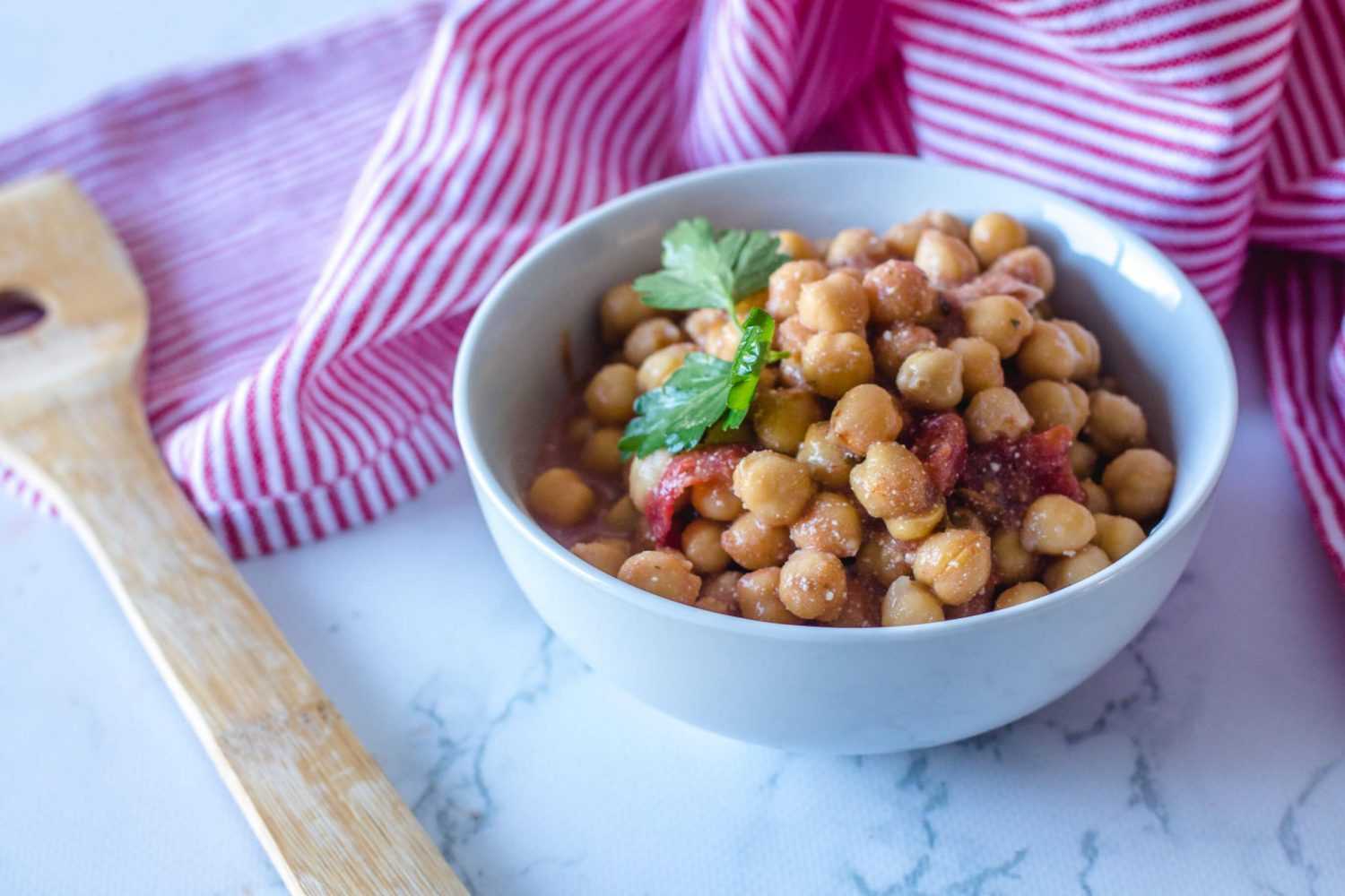 Chana masala with chickpeas, chopped tomatoes, parsley and spices in white bowl