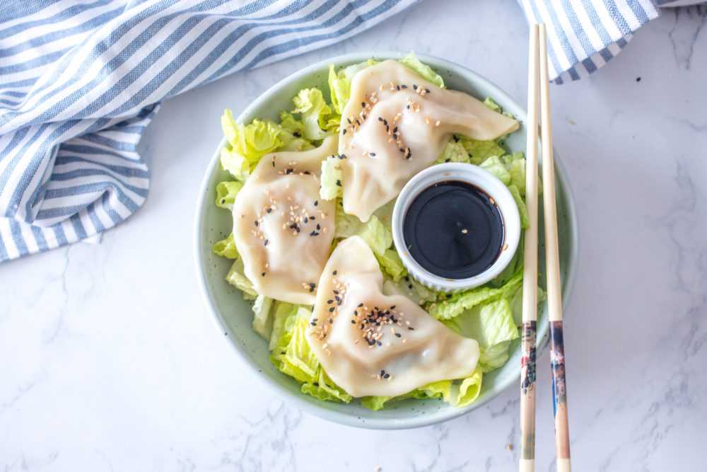 Steamed Dumplings over shredded lettuce topped with black and white sesame alongside soy sauce and chopsticks