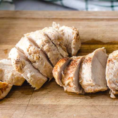 Chicken breast sliced topped with salt and paprika on a cutter board