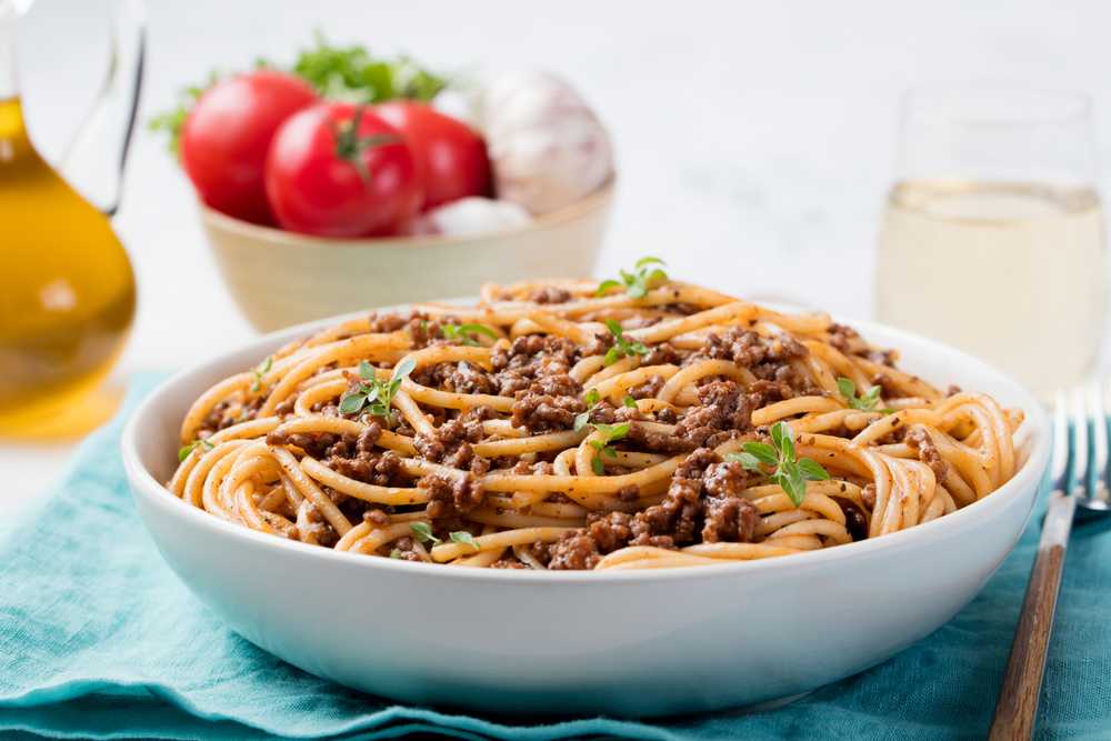 Gluten free spaghetti with ground beef, tomato sauce and mint leaves on top in a white bowl