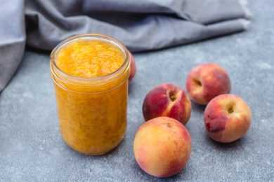 Peach jam in a jar with whole peaches on side