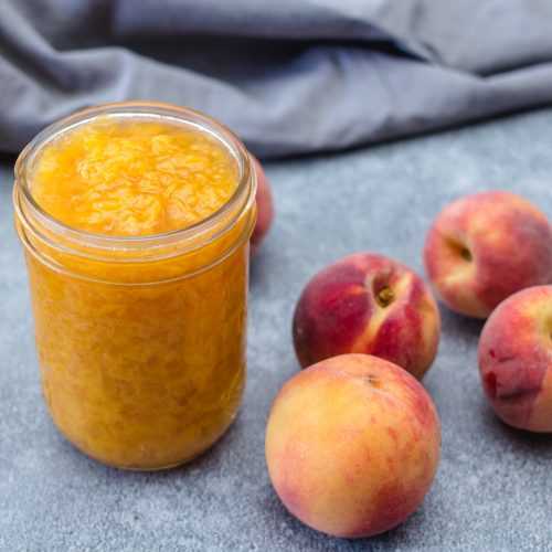 Peach jam in a jar with whole peaches on side