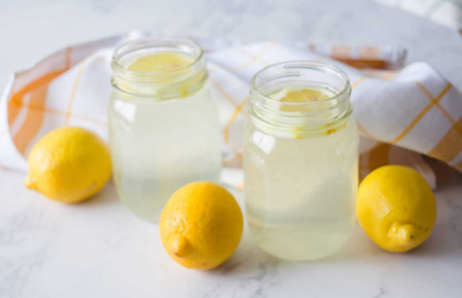 Limoncello in two jars topped with lemon slices with lemons on side