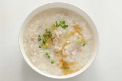 Congee made of rice topped with chicken pieces, ginger and scallion in white bowl