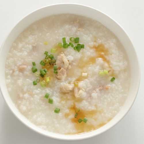 Congee made of rice topped with chicken pieces, ginger and scallion in white bowl