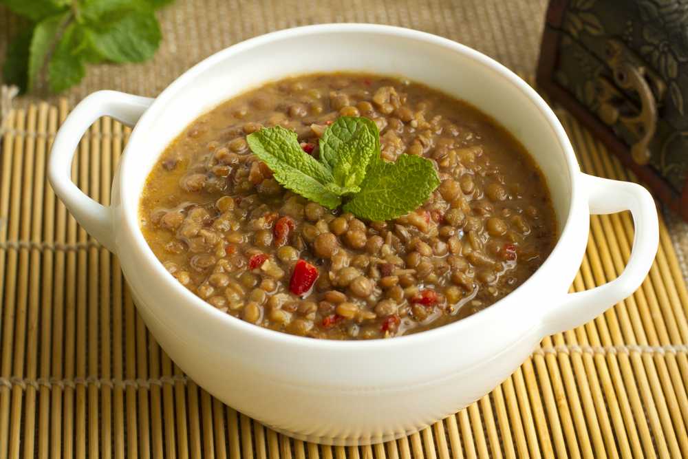 Brown lentil soup topped with red pepper flakes and mint in white bowl