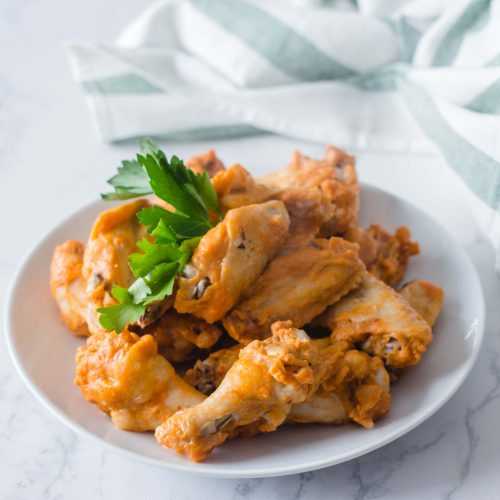 chicken wings with sauce topped with parsley leaves in a white plate
