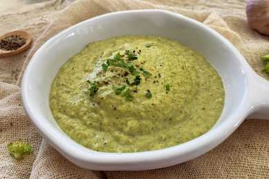 Blended broccoli soup with chopped parsley and black pepper on top in white bowl