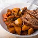 Venison roast with roasted potatoes, onions and spices in white bowl