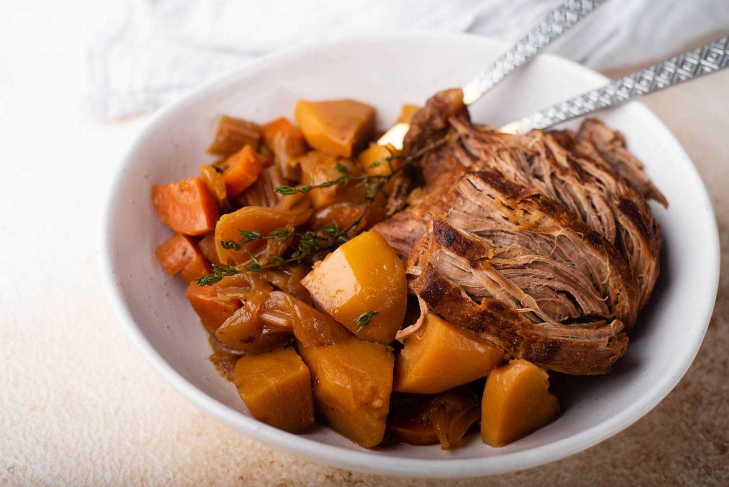 Venison roast with roasted potatoes, carrots, onions, thyme and spices in white bowl