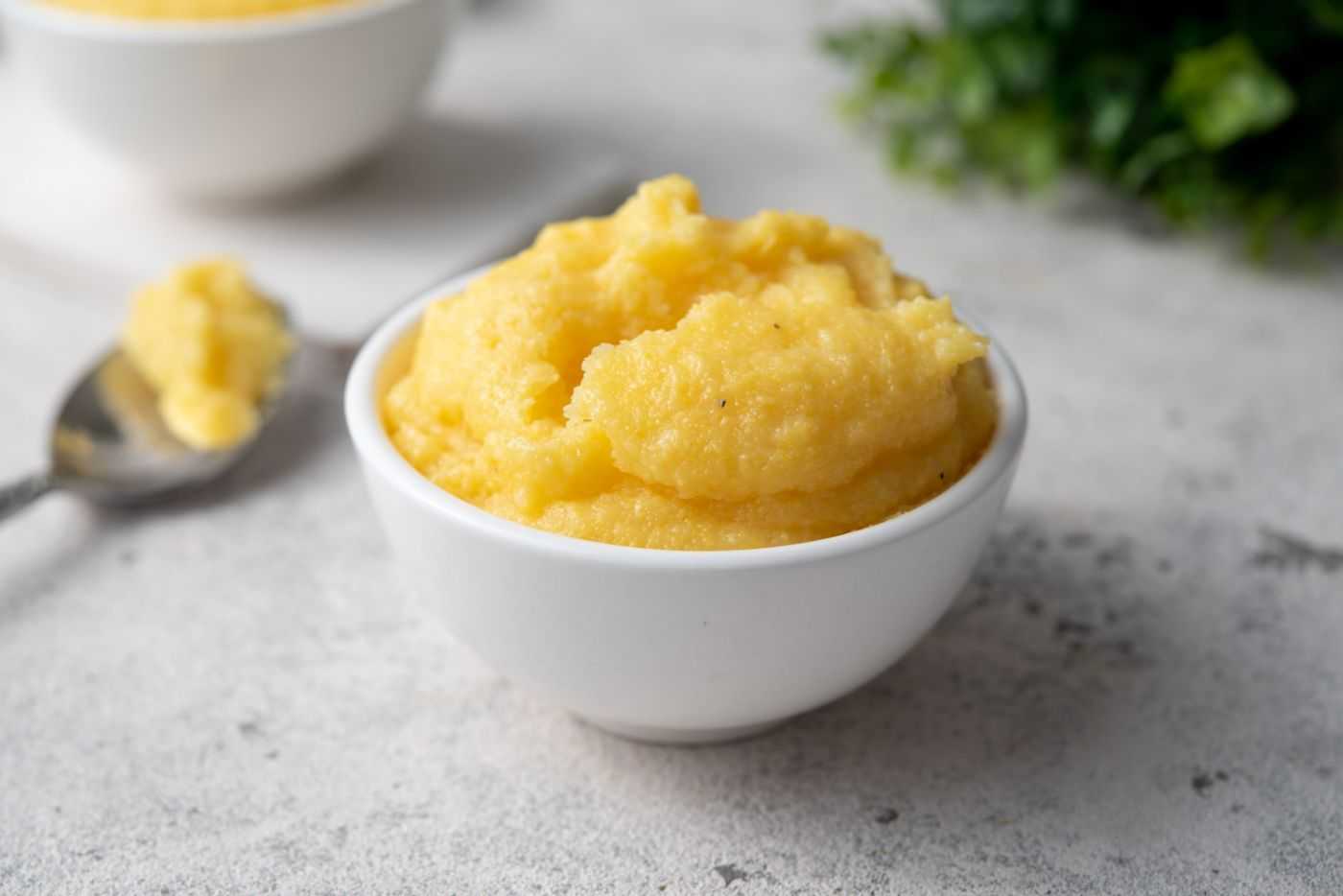 Polenta inside white bowl with spoon filled with polenta
