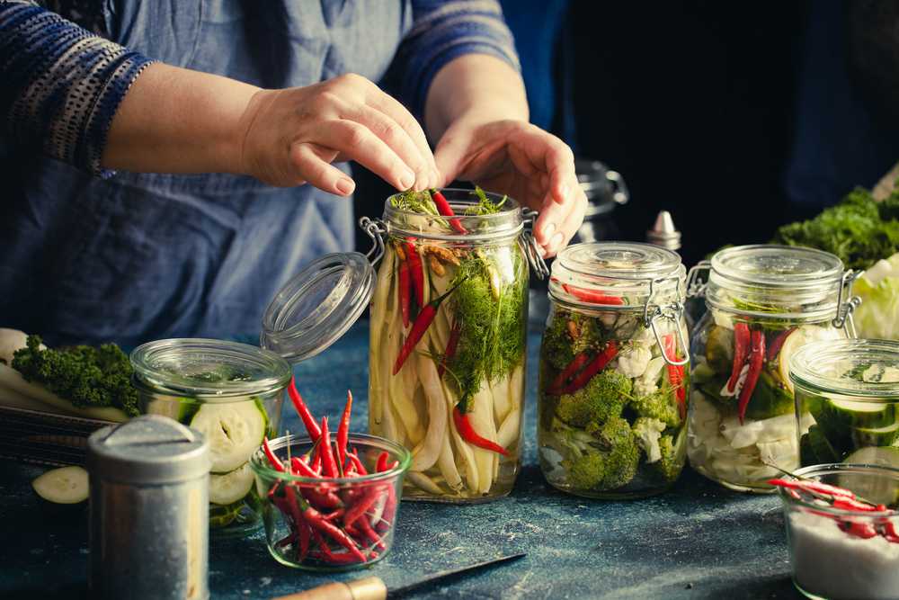 woman put vegetables inside jars that full with water in order to can them 