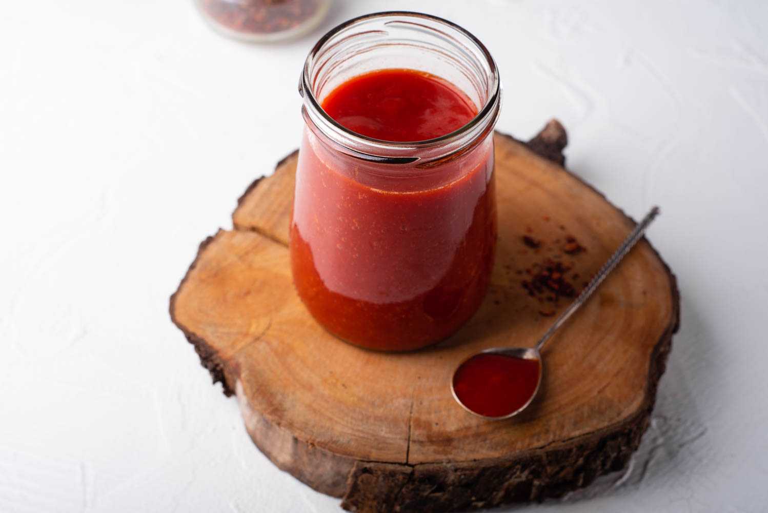 red tabasco sauce in a jar with s spoon aside filled with the sauce on a wooden piece