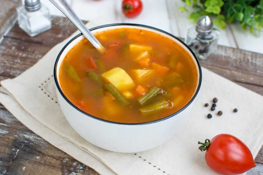 Red soup filled with green bean, carrot and potato cubes, corn and cherry tomatoes