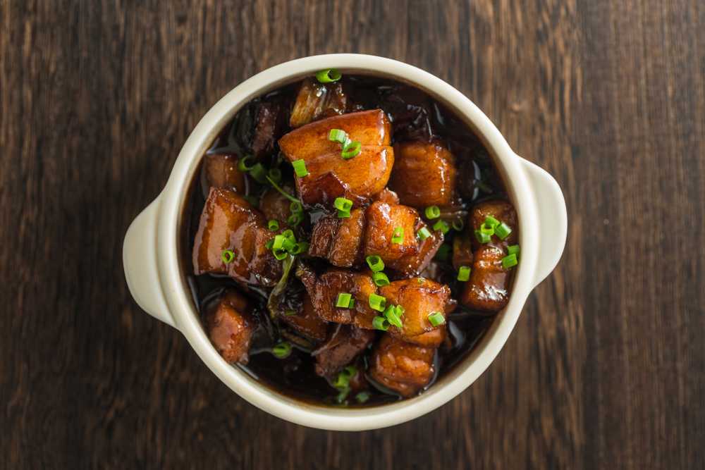 Pork cubes in brown caramel sauce with chopped scallion on top in white bowl top view