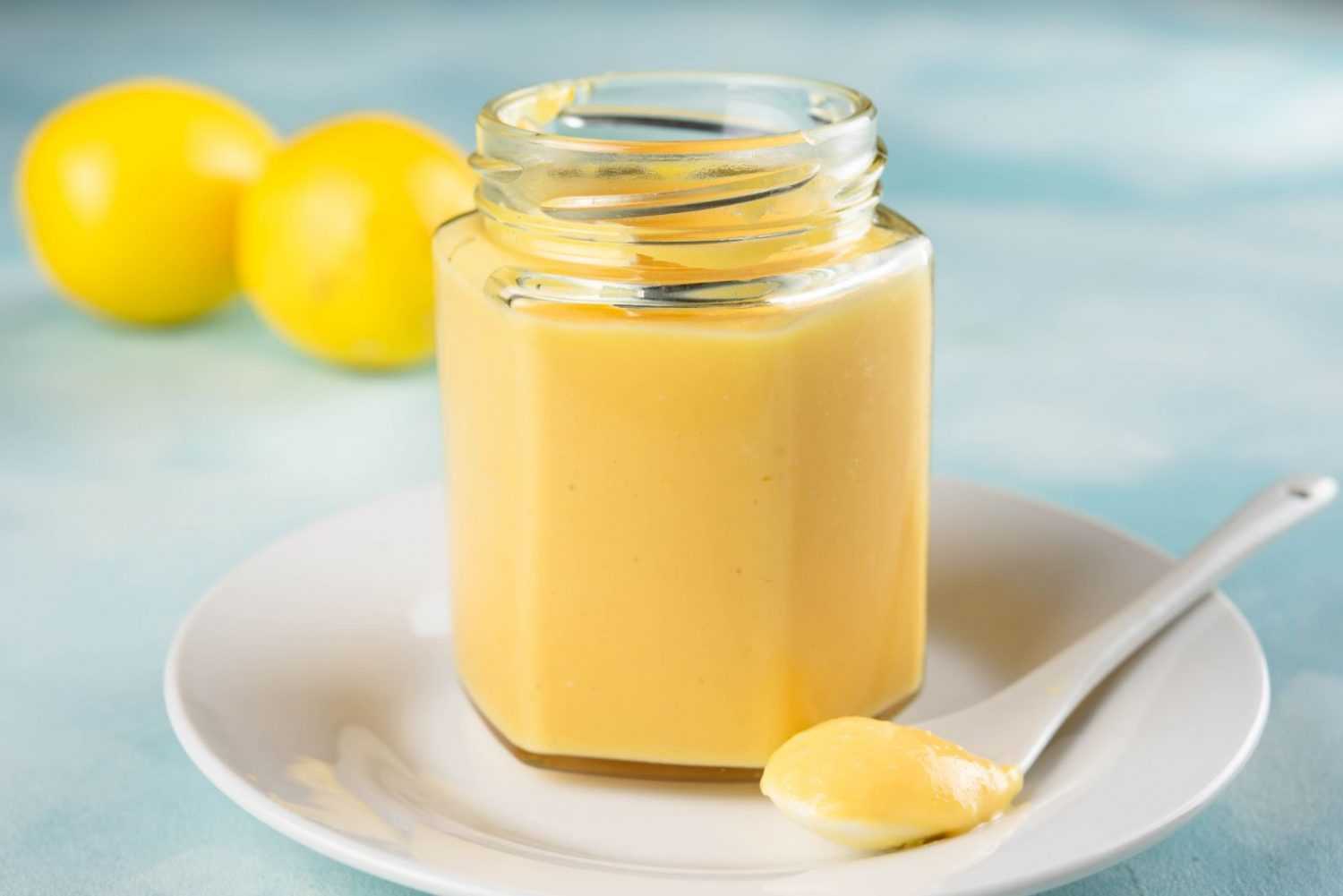 Lemon curd in a jar with a spoon holding a some and fresh lemons on side