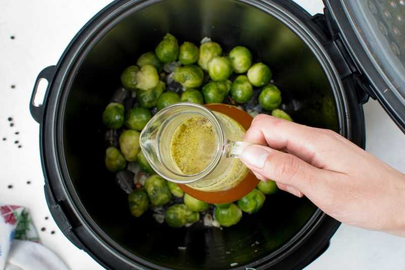 adding chicken stock into a pressure cooker filled with brussel sprouts 