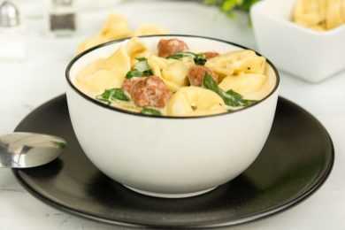 Tortellini soup with sausage, basil, spinach, cheddar cheese and spices in white bowl